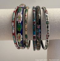 Front view of six cloisonné bangles on display rack showing colorful floral enameling.