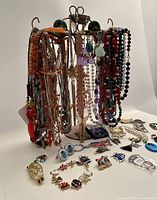 Wide view of vintage costume jewelry lot displayed on and around a jewelry holder showing multiple beaded necklaces, earrings, pins, a Christmas charm bracelet, and a ceramic Santa brooch.