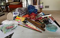 Wide shot of the craft supplies lot shown on floor including yarn, paint brushes, wooden spindles, Rit dye, buttons, and sign panel.