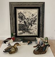Photo of framed Montana Marble Mallard Ducks artwork and five duck figurines positioned in front of it.