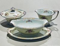 Sugar bowl, creamer, and gravy boat with attached plate showing floral and gold trim pattern matching set