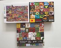 Top-down photo showing all three boxed puzzles: Kodak Premium Cork Board Hearts, Yinsheng Famous Candies, and Best Kid Books of All Time puzzles, all labeled 1000 pieces.