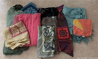 Overview photo showing the entire collection of scarves and shawls laid out on a carpeted floor, displaying a variety of colors and patterns.