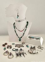 Full lot laid out and displayed on white bust and flat surface showing all jewelry items including necklaces, earrings, brooch, and ring.