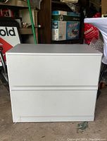 Front view of light gray two drawer laminate chest showing flat front drawer surfaces without handles on a concrete floor in garage setting.