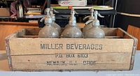 Front and inside view of wooden crate with six seltzer bottles showing the Miller Beverages stencil