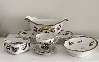 Front view of antique Limoges gravy boat with matching tray, finger bowl, demitasse cup with saucer, and small ashtrays showing exterior decoration and size relation