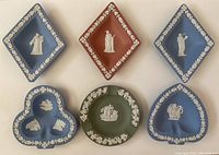 Six jasperware ashtrays and trays in blue, red, and green with white reliefs, arranged on a flat surface showing front designs.