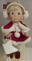 Front view of the 1992 Christmas Angel Lee Middleton vinyl doll wearing red velvet with white faux furry trim skating outfit holding white skates.