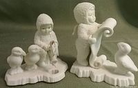 Photo of two Dept. 56 Snowbabies figurines on a neutral background showing Puffin Fishing and Puffin Reading with puffin birds on snow-like bases.
