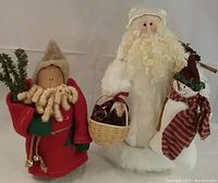 Two hand made cloth Santa dolls, one in red with evergreen and bells, one in white with basket and snowman, front view