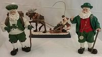 Photo shows three Santa figurines: two Clothtique Irish Santas and one David Frykman resin statue with Santa riding a moose-pulled sleigh.