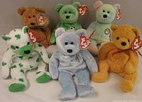Photo of six vintage Ty Beanie Bears including Issy, Poopsie, Clover, Kicks, Birthday, and an unnamed bear. All have hang tags attached. Bears are arranged sitting on a surface against neutral background.