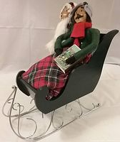 Side angled view of Byers Choice Carolers couple seated in black wooden sleigh with metal runners.