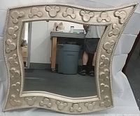Front view of the square mirror showing the silver frame with Mickey Mouse head icons embossed around the edges and clear mirror glass reflecting a background scene.