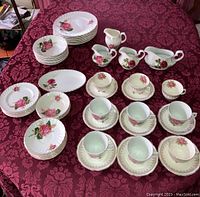 Full set arranged on table featuring dinner plates, teacups with saucers, gravy boat, creamers, serving plate, cake plates, dessert plates