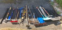 Full view of all garden and outdoor tools laid out on a grassy surface, showing various rakes, shovels, hoes, scrapers, and brooms.