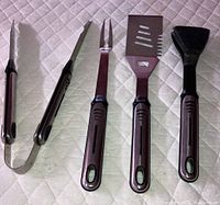 Full view of barbecue tool set: tongs, fork, spatula and grill-cleaning tool with scraper and brush