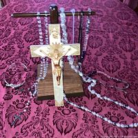 Necklaces draped over wooden display stand, crucifix prominently centered, with beaded necklaces and tiara surrounding it.