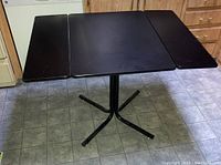Top front view of black extendable table with both wings unfolded showing entire tabletop surface and base.