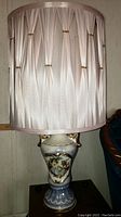 Full view of porcelain table lamp on wooden table with lampshade and decorative gold details