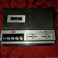 Front view showing cassette compartment with auto stop, metal control buttons, volume and tone sliders.