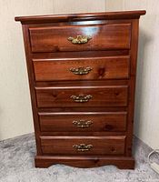 Front view of the walnut wood chest with five drawers showcasing brass handles and wood grain.