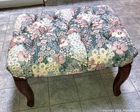Top and angled view of rectangular floral upholstered foot stool with tufted cushion and dark wooden curved legs.