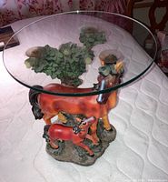 Full view of the painted porcelain horse and colt sculpture with attached clear round glass tabletop showing the horse and colt figure on a textured base with a tree model.