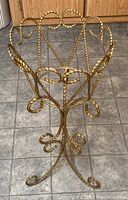 Full view of gold painted wrought iron planter frame standing on tile floor, showing twisted metal design and legs.