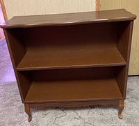 Front view of the wooden low shelf unit with two shelves, showing the decorative molding and wear near the base.