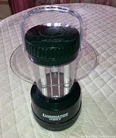 Green and black Dorcy Luminator emergency lamp with a transparent handle shown unlit on a cloth surface.