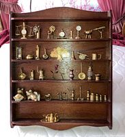 Full view of wooden display cabinet with five shelves holding various small brass figurines including animals, timepieces, scientific instruments, and decorative objects.