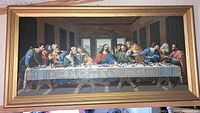 Framed paint-by-numbers depiction of The Last Supper on a wall, showing Jesus and his disciples at a long table, with wooden frame.