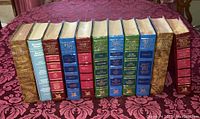 Eleven hardcover Reader's Digest Condensed Books volumes displayed upright in a row showing various colored spines with gilt titles. Books show wear and age on covers.