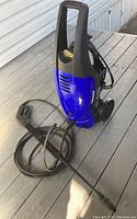 Blue and black Simoniz S-1500 pressure washer unit with attached hose and wand, standing on deck surface.