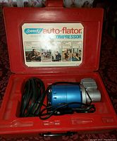 Red plastic case open showing blue and metallic mini compressor unit with attached black cable and inflator hose packed inside.