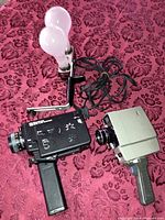View of the Sears Easi-Load camera and GE 400W movie light apparatus laid on fabric surface, showing camera lens, pistol grip handle, and lamp bulbs