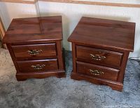 Photo showing both twin walnut bedside tables side by side on carpeted floor near a wall.