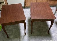 Photo of two matching wooden side tables with scalloped edges and brass handle detail on drawer.
