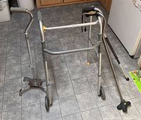 Photo showing the walker with two front wheels, taped and not folding, alongside two canes: one quad cane with four feet and one single-foot cane.