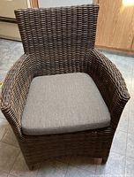 Front view of the brown wicker lounge chair with grey cushion, showing the woven texture and armrests.