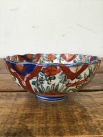 Side view of antique Japanese Imari hand painted bowl showing red, blue, green floral and patterned decoration on scalloped rim and footed base