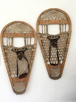Pair of vintage wooden snowshoes mounted on a wall, showing entire shape and size with leather straps intact.