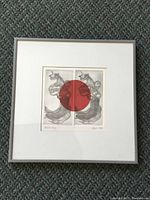 Framed matted artwork featuring two symmetrical abstract figures with a large red circle at center, signed and dated 1972, displayed in entirety.