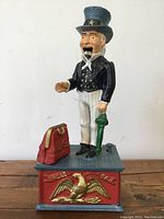 Front view of the cast iron Uncle Sam piggy bank with base, red bag, and eagle detail.