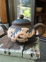 Side view of brown Yixing clay teapot showing raised white dragon design on body and round lid with knob.