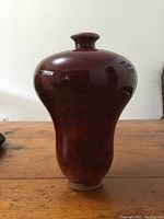 Front view of red glazed vase showing bulbous shape and glossy finish