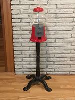 Full view of vintage gum ball machine standing on hardwood floor against brick wall.