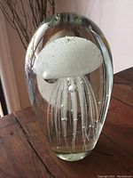 Heavy clear glass jellyfish paperweight showing white jellyfish figure with bubbles inside.